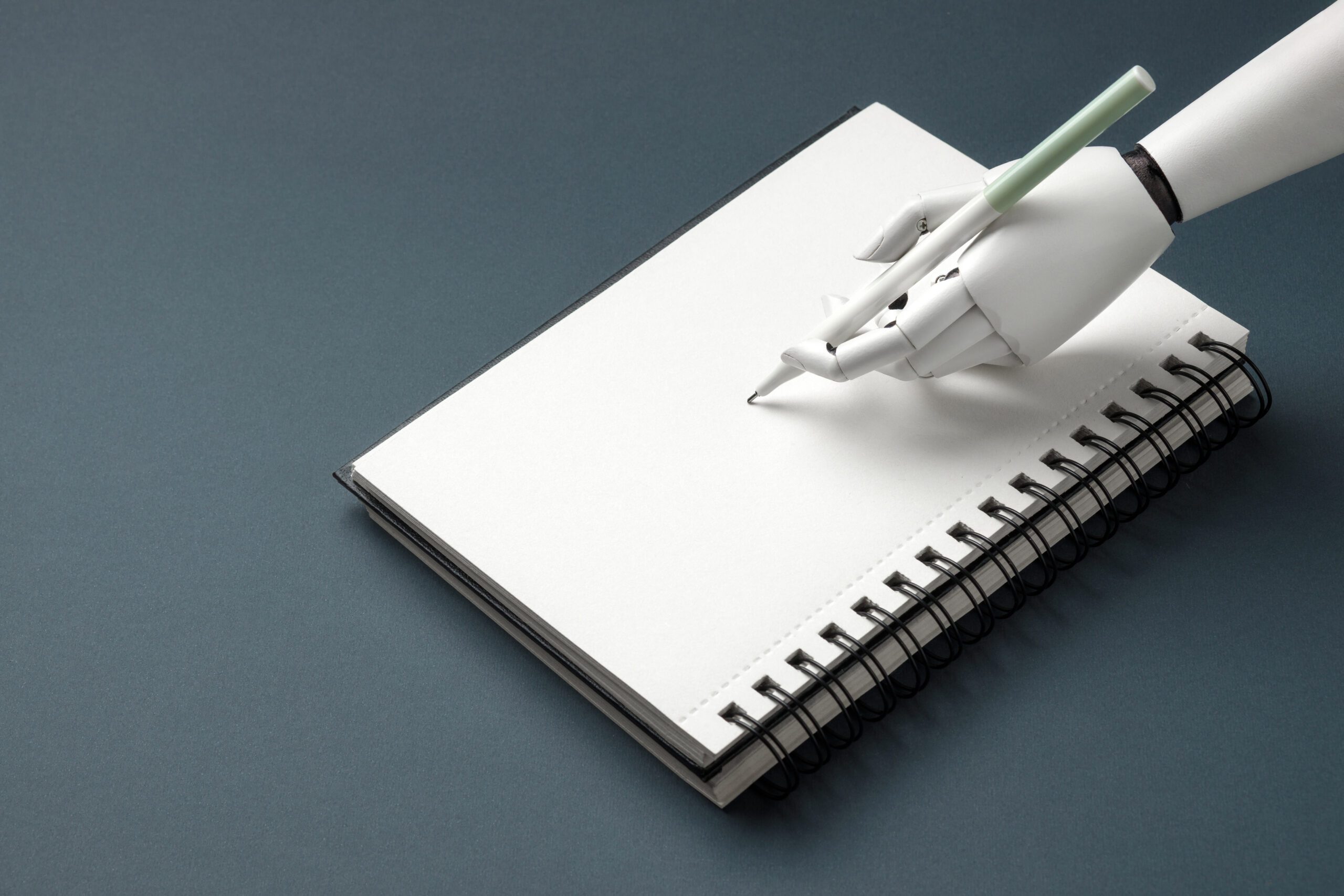 White robotic hand holding a pen, ready to write in an open blank spiral notebook on a dark background. Concept of artificial intelligence, creativity and text generation.